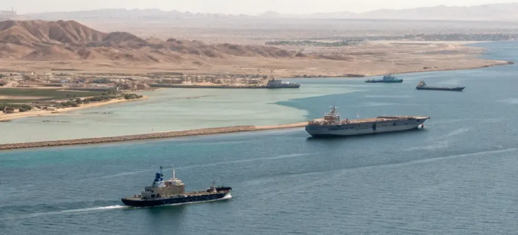 Naval and commercial vessels moving through Bab el-Mandeb strait near coastline, illustrating regional spillover risk in Red Sea shipping attacks news today and maritime chokepoint security
