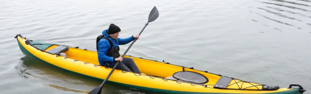 Paddler using a double-bladed paddle in an inflatable kayak, highlighting control differences in inflatable kayak vs inflatable canoe design
